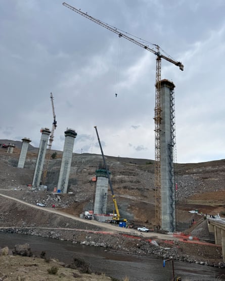 Stone pillars under construction on a hillside. Cranes are situated alongside two of the pillars.
