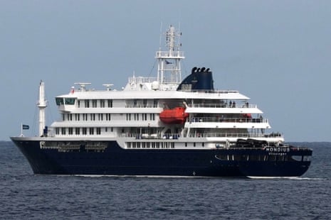 The MV Hondius cruise ship with multiple decks and a red tender boat sails on calm water.
