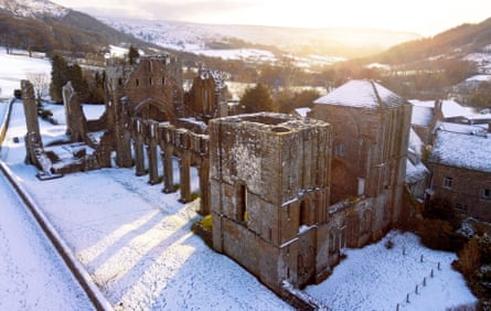 Ruins of a priory in winter set in a valley with sun streaming in.