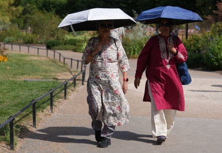 Two people walking along a park footpath under the shade of umbrellas
