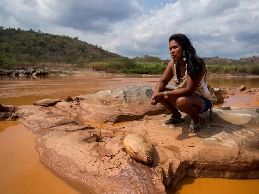 Uma mulher brasileira na margem de um rio laranja altamente poluído