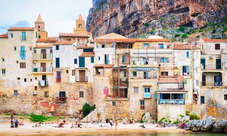 People on beach in front of buildings with mountains behind