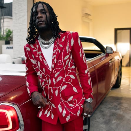 Burna Boy photographed in Lagos earlier this month wearing a red suit and standing by a red open-top class=