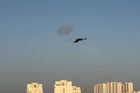 A bird flying as smoke is seen in the sky.