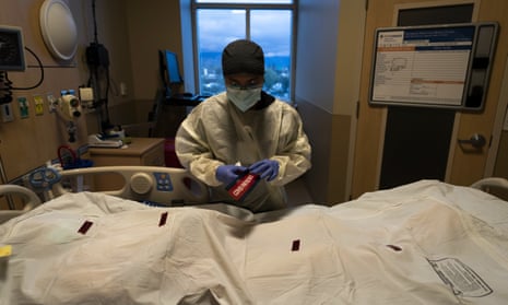In a small hospital room, a nurse in protective gear attaches a sticker reading "COVID Patient" to a white body bag containing a patient who died of coronavirus.