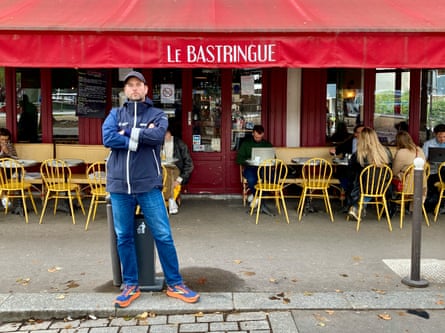 Man in baseball cap and jeans standing outside a restaurant in Paris