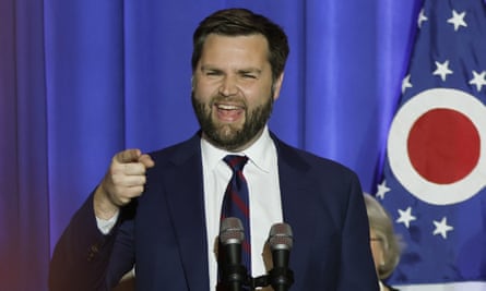 Young middle-aged white man in suit with brown hair and full beard, smiling and speaking and gesturing at lectern.