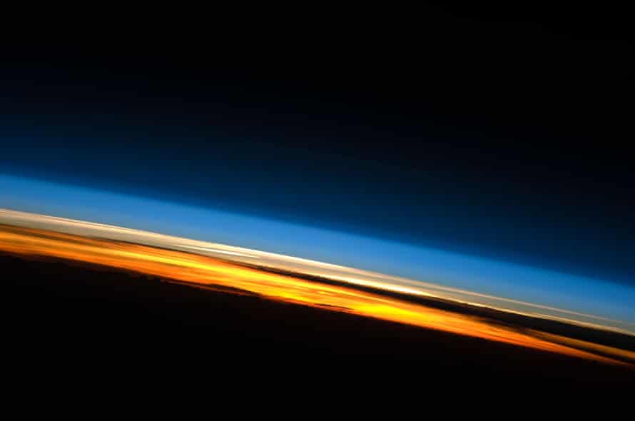 Sunset over the Indian Ocean.  Above the obscured surface of the earth, a brilliant color gamut indicates approximately the layers of the atmosphere.  Deep oranges and yellows are visible in the troposphere that extends from the earth's surface to 6-20 kilometers high.  The pink to white region above the clouds appears to be the stratosphere;  this atmospheric layer usually has little or no clouds and extends to about 50 kilometers above the earth's surface.  Above the stratosphere, blue layers mark the upper atmosphere as it gradually fades into the blackness of outer space.