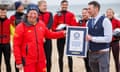Chris Lewis receiving his award from the Guinness World Records’ managing editor Adam Millward on beach with other lifeguards in background