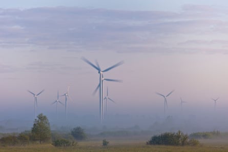 The blades of wind turbines emerge from the mist in rural Poland