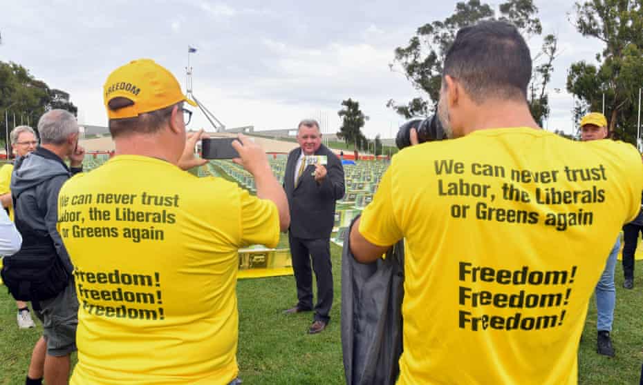 People in yellow campaign t-shirts take photos of United Australia Party Member for Hughes Craig Kelly in front of fake 100 Australian dollar notes at a United Australia Party budget event outside Parliament House in Canberra