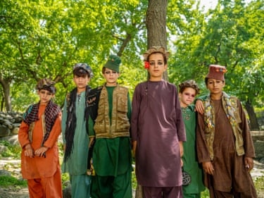 A group of seven teenage men face the camera in strikingly coloured robes and headgear