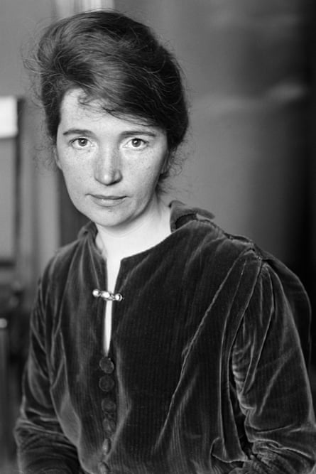 A young woman looks directly at the camera in this black and white photo; her hair is piled into a high french roll, and she is wearing a dark velvet tunic with a barrette-style brooch pinned across the front vent.