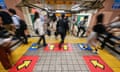 A blurred picture of people passing through a station with arrows pointing in different directions on the floor.