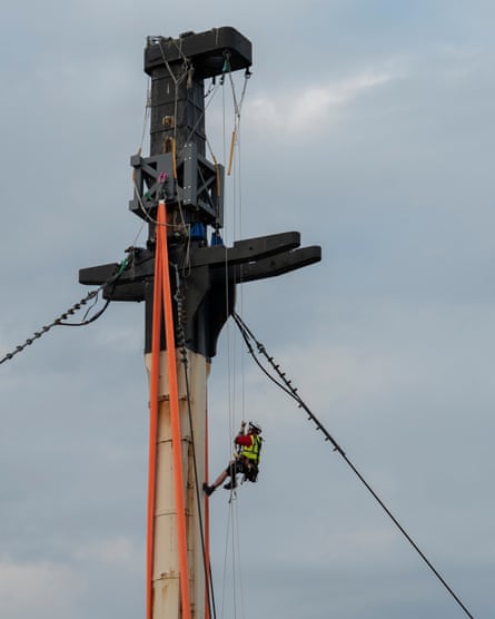 Sheldon attached to ropes, dangling off the side of the mast near the top