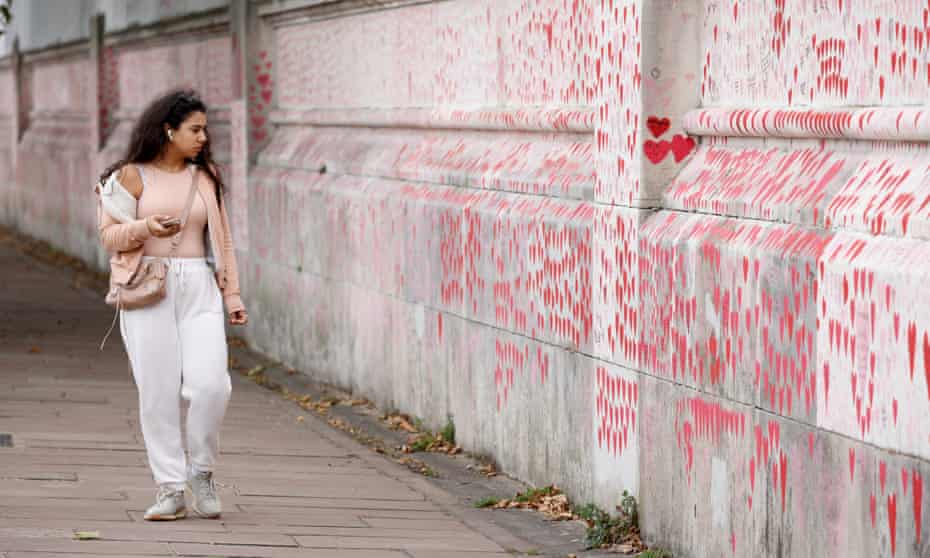 A young woman with black hair at the National Covid Memorial Wall in London, looking at red hearts drawn on the wall.