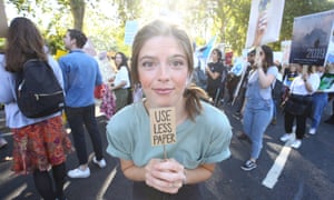 A young climate striker with a tiny placard reading ‘Use less paper’