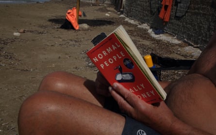 A tourist reading a Sally Rooney novel on a beach in Greece