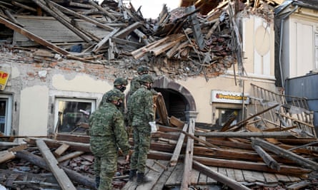 Croatian Soldiers walk on wreckage next to damaged buildings in Petrinja, Croatia.