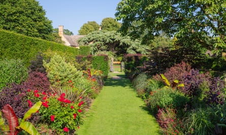 Red borders either side of a long grass pathway at Hidcote.