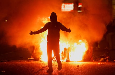 A rioter is silhouetted at night with flames in the background