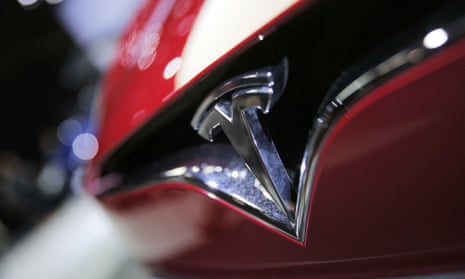 A close-up of the red and chrome front bumper of a car, with the Tesla T logo.