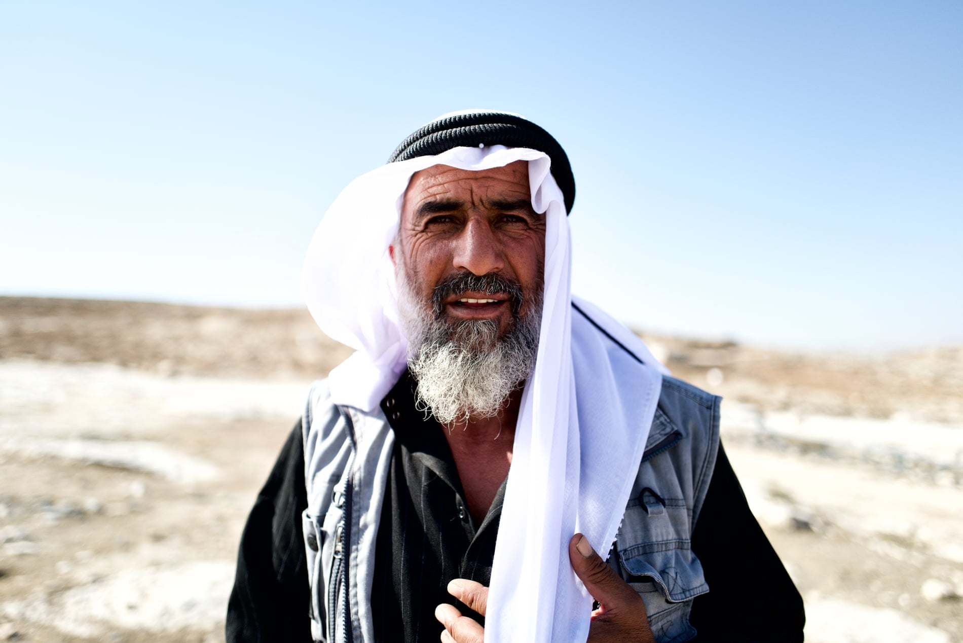 A man in a keffiyeh in a desert looks at the camera