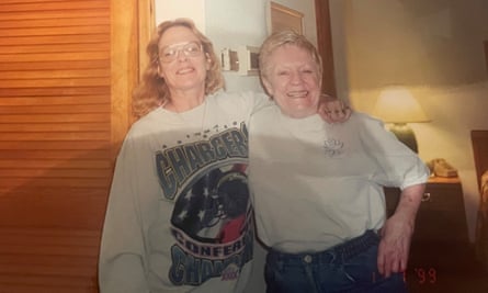 Photo of a color photo, of a younger woman in a sweatshirt with her arm around the neck of an older woman, both smiling, in a bedroom.