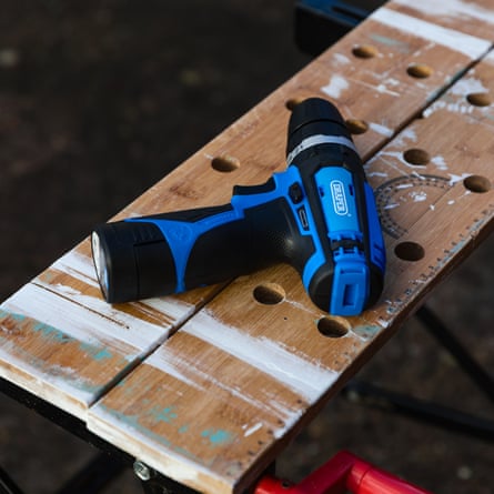 The Draper 12V Combi Drill 70256 us laid flat on a wooden workbench. The drill is electric blue and black.