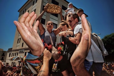 Hands envelope a group of people partaking in a ritual, one woman holding up a loaf of flatbread