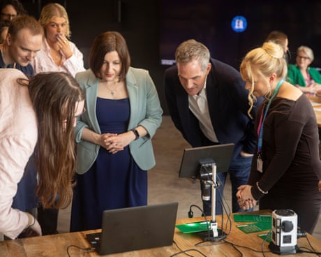 Image 3: Peter Kyle leaning over a looking at a computer screen with fellow MP Bridget Phillipson to his right and several other people around.