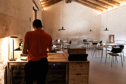 A man stands at a desk in a sparsely furnished restaurant in a converted barn