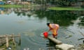 A woman in a pink and orange sari uses a bucket to collect water from a pond