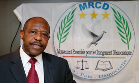 Paul Rusesabagina standing before a banner showing a dove, olive branches, scales and a book. The slogan says in French: justice, peace, democracy