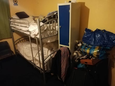 Two bunk beds in a room next to a small cupboard with personal belongings piled up all around it