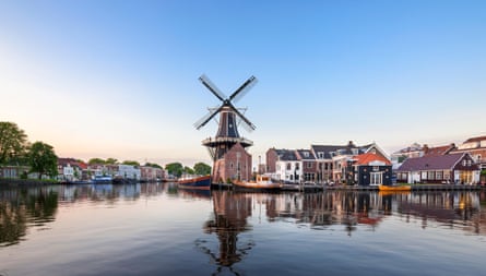 A river with a windmill and other buildings in the distance