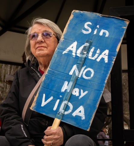 An older woman holds a hand-painted sign saying: ‘Sin agua no hay vida’.