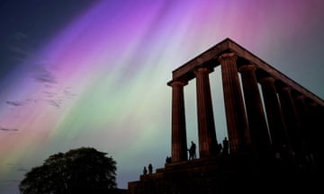 Pillared monument with people in silhouette against northern lights