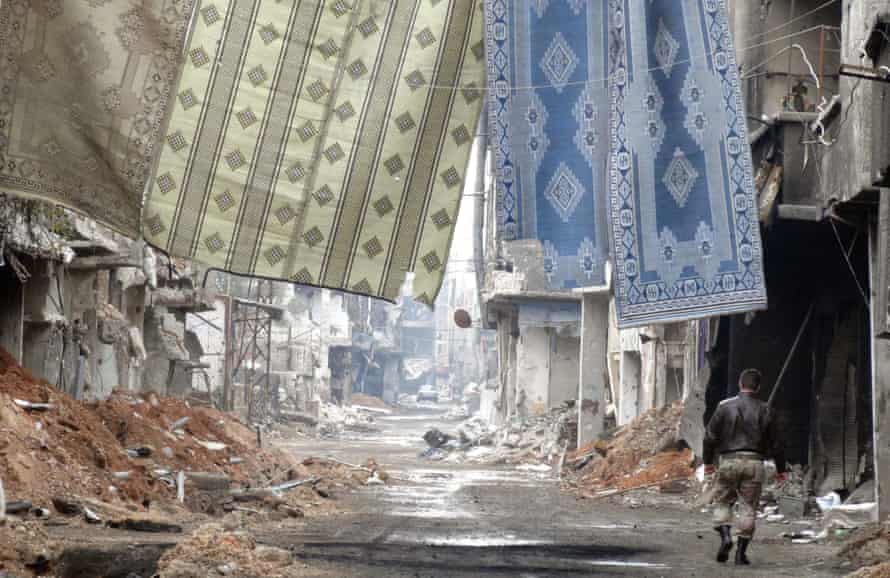 A Syrian regime militiaman walks underneath anti-sniper screens on a devastated street near the front line in Tadamon, January 2014