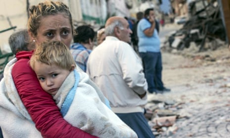 A woman holds a child as they stand in the street following an earthquake in Amatrice