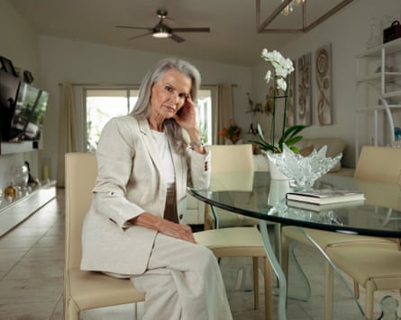 A woman with blond hair in a white suit sitting at a glass table