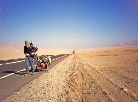 With a scarf wrapped around his head, he drags his trolley along a road across a sandy desert devoid of life