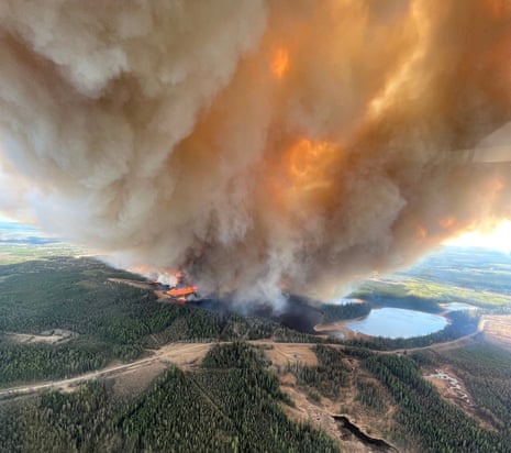 A column of smoke and flames rises from a forested area in this aerial view.