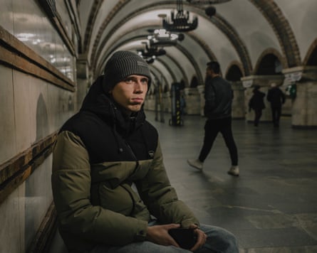 Seated 21-year-old Ukrainian man dressed for the cold on a Kyiv metro concourse.