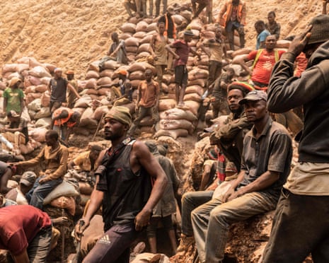 Exhausted looking miners sit below an excavated cliff strewn with sacks.