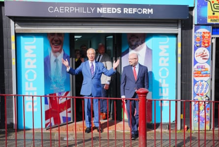 Two men stand outside a shop front with signs reading 'Caerphilly needs Reform'.