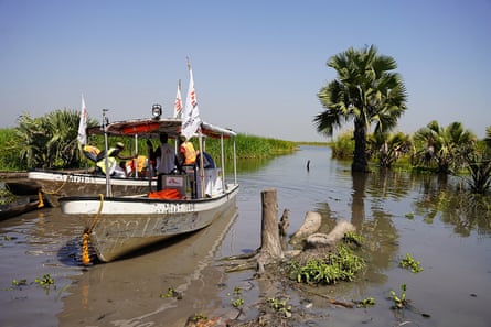 A boat with MSF flags is loaded with white cardboard boxes containing vaccines.