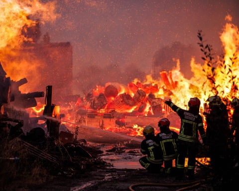 Firefighters look on at large flames