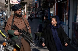 A Taliban fighter stands guard as a woman walks past him in Kabul