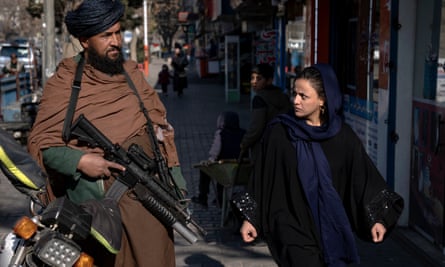 Un combattant taliban monte la garde devant une femme qui passe à Kaboul, en Afghanistan, en décembre 2022.